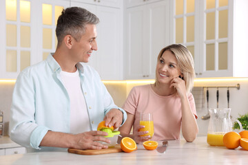 Happy couple with juicer and fresh products making juice at white marble table in kitchen
