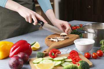 Healthy food. Woman cutting champignon at grey table, closeup