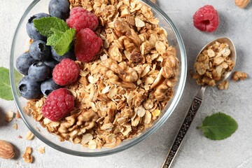 Tasty granola with berries, nuts and mint on grey table, flat lay