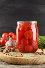 Tasty pickled tomatoes in jar and spices on wooden table