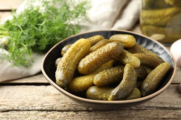 Pickled cucumbers in bowl on wooden table, closeup