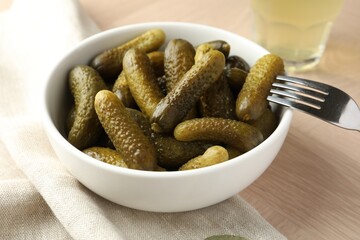 Pickled cucumbers in bowl and fork on wooden table, closeup