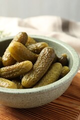 Pickled cucumbers in bowl on wooden board, closeup