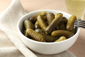 Pickled cucumbers in bowl and fork on wooden table, closeup