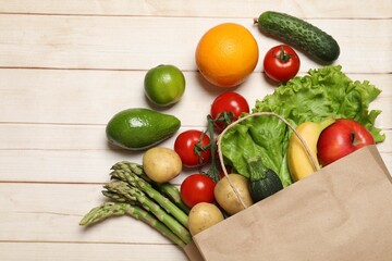 Vegan food delivery. Paper bag with different fresh vegetables and fruits on light wooden background, flat lay