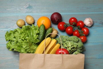 Vegan food delivery. Paper bag with different fresh vegetables and fruits on light blue wooden background, flat lay