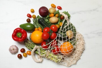 Vegan food delivery. Net bag with different fresh vegetables and fruits on white marble background, flat lay