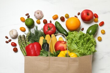 Vegan food delivery. Paper bag with different fresh vegetables and fruits on white marble background, flat lay