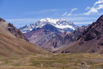Closeup photo of the highest mountain in South America, Aconcagua, with blue sky, rocky mountains and a river leading the way.