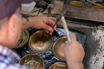 A man is working on a project with a brush and a hammer. He is creating a design on a piece of metal