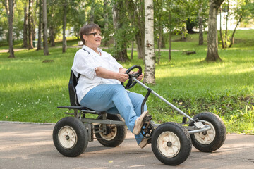 An elderly woman rides a toy car.