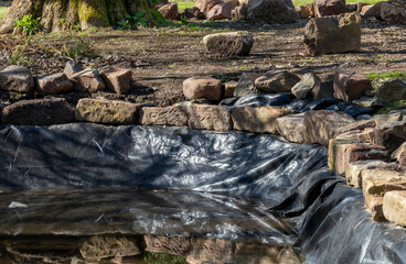 Building ornamental garden water pond with black liner and edging rock blocks
