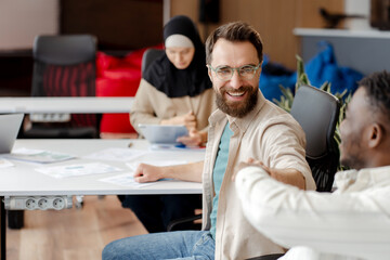 Obraz premium Business people, smiling employees shaking hands during meeting in modern office
