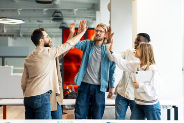 Diverse business team giving high five, celebrating success in modern office