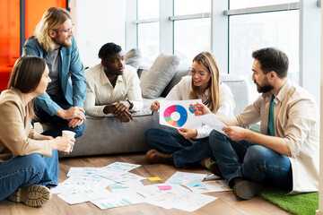 Team of young professionals is brainstorming new project using data visualization on floor in office