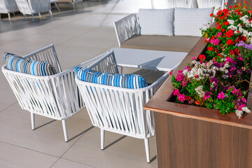 Outdoor patio table and chairs with flower decoration in hotel lobby. Restaurant terrace scene featuring white table and chairs