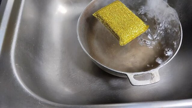 Una esponja amarilla flotando y movi&eacute;ndose en un caldero que le cae mucha agua en un fregadero