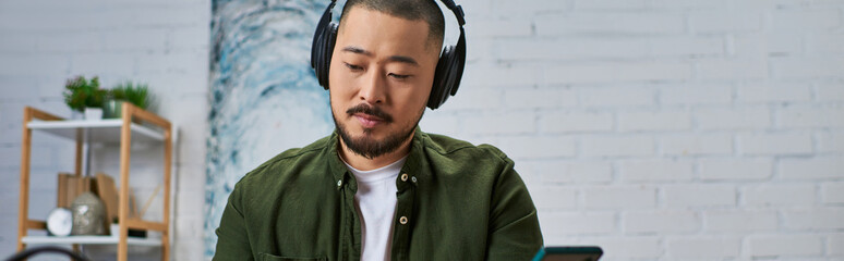 A handsome Asian man in casual attire, engrossed in his music, plays an instrument in a modern...