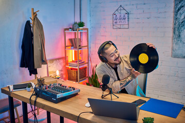 An Asian man podcasting in his studio, holding a vinyl record.