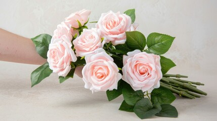 A persons hand holds a bouquet of pink and white roses against a white wooden background