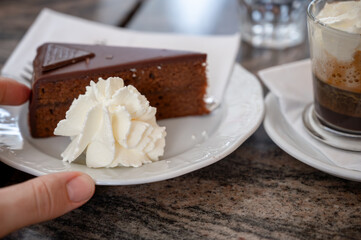 Vienna, Austria, August 18, 2022. Nice shot of a Viennese specialty: a nice slice of sachertorte served on a plate with some whipped cream next to it. The hand grabs it.