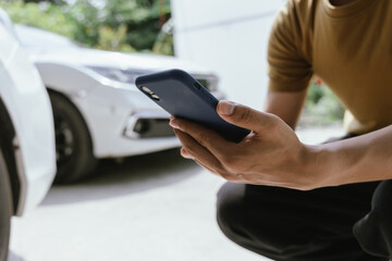 A young adult man, holding a smartphone, takes a photo of his dented car after an accident. An insurance agent with a clipboard examines the damage, preparing a claim report.