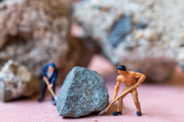 A miniature worker worker drilling a big rock . Themes of perseverance, strength and labor.