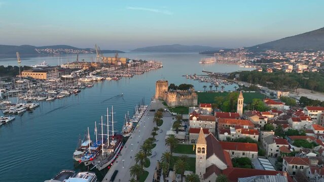 Drone video at sunrise with the beautiful old buildings and marina with boats of the old town of Trogir in Croatia, the Adriatic coast.