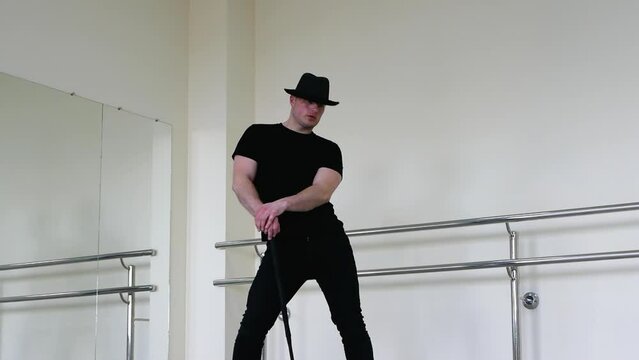 Cabaret or jazz dance with a cane in the studio. A young man in a black gangster hat and black clothes dances driving blues with a stick in his hands
