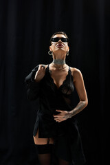 A woman in black lingerie and sunglasses poses against a dark background.