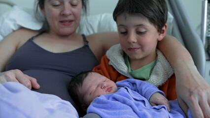 Obraz premium Sibling looks lovingly at newborn baby while sitting beside their mother, highlighting the tender bond between siblings and the beginnings of a lifelong loving relationship