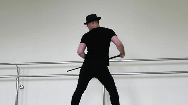 Cabaret or jazz dance with a cane in the studio. A young man in a black gangster hat and black clothes dances driving blues with a stick in his hands.