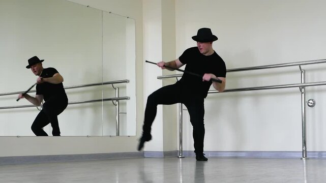 Jazz dance or caberet rehearsal in the studio with a cane, a young guy in a gangster hat. Creative dance blues man, in black clothes with a stick in his hands.m