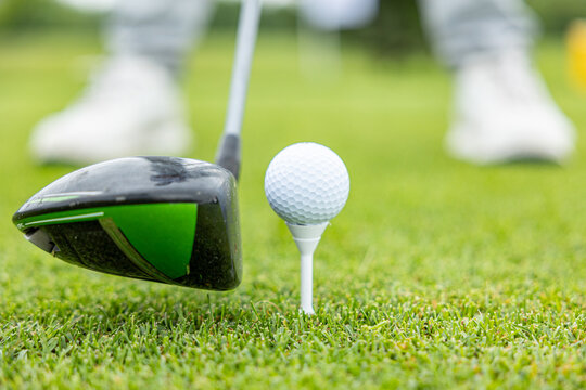 Front view of golf ball on tee with golf drivers at golf course.