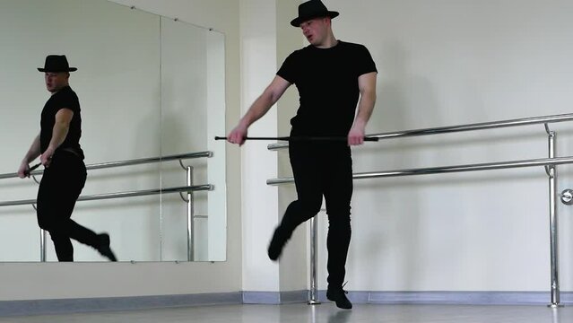 Jazz dance or caberet rehearsal in the studio with a cane, a young guy in a gangster hat. Creative dance blues man, in black clothes with a stick in his hands
