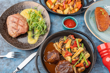 A table served with dishes of meat, vegetables, potatoes and herbs.