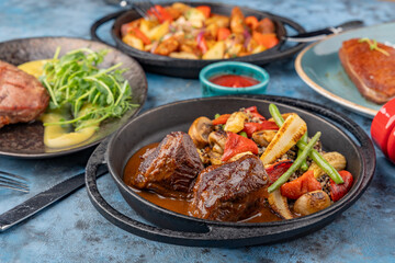 A table served with dishes of meat, vegetables, potatoes and herbs.