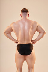 Medium full shot of bodybuilders strong back muscles and glowing skin on neutral background. Young...