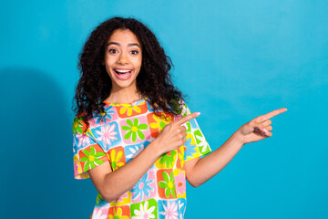 Photo of adorable excited girl wear flower print t-shirt showing two fingers empty space isolated blue color background