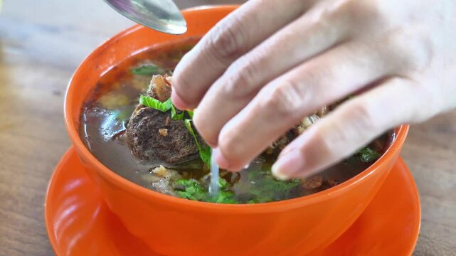 a person holding a spoon and squizee a lime over a bowl of clear soup in restaurant in Indonesia