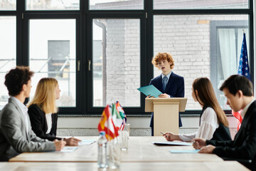Teenagers listen attentively at Model UN conference as peer gives speech.