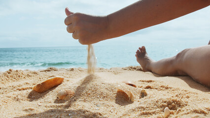 Woman sits on a sandy sea beach on a sunny summer day and sifting sand through her hand onto a small slide