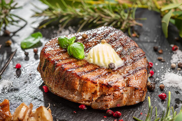 Grilled delicious ribeye steak with melting piece of butter on it. Steak is on black slate serving plate. Flat lay.