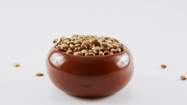 Feijao cru caindo em uma tigela de barro marrom em fundo branco