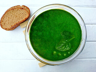 Spinach green peas cream soup on white wooden background. Spring green vegetable (spinach, broccoli, peas) soup pure in glass bowl. Tasty vegan healthy food - spinach soup on table for lunch or dinner