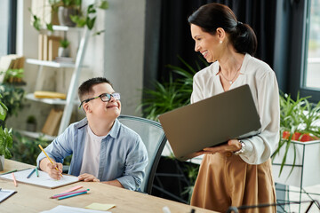 A mother smiles at her son as he works on a drawing at the office, demonstrating inclusivity and...