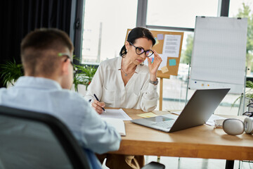 A mother works at her desk in an office, while her son sits beside her.