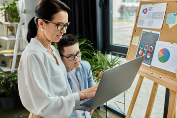 A mother works on her laptop while her son with Down syndrome looks on, showcasing a supportive and inclusive environment.