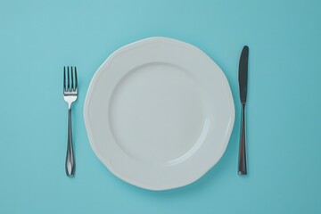 
empty white plate with knife and fork on blue background