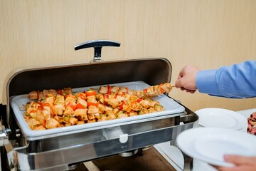 A person is taking food out of a buffet tray